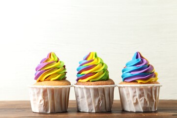 Delicious cupcakes with colorful cream on wooden table against white background, closeup