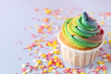 Delicious cupcake with colorful cream and confetti on light table, closeup. Space for text