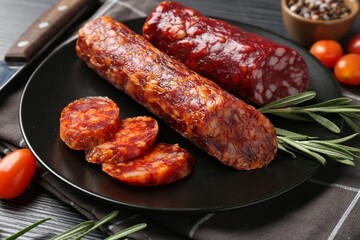 Cut smoked sausages, rosemary and tomatoes on black wooden table, closeup