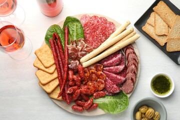 Different smoked sausages and other snacks served with wine on white table, flat lay