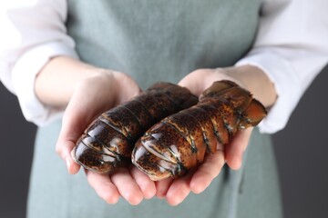 Woman with raw lobster tails on dark grey background, closeup