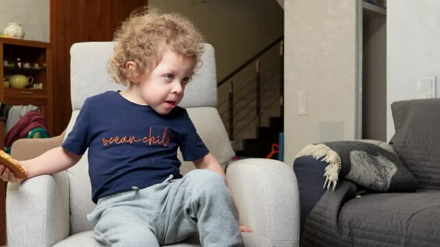 Little boy 3 years old in chair watching cartoon in room and eating biscuits. Children and lifestyle. Emotional Intelligence. 