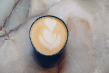 A cup of fresh delicious cappuccino coffee with beautiful latte art on marble background, top view.  Morning scene with hot drink.