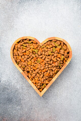 Heart-shaped bowl with dry cat food. On a gray concrete background. Top view.