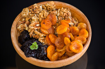 Prunes, dried apricots and nuts in a wooden bowl on a dark background