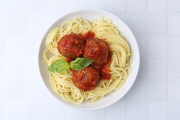 Delicious pasta with meatballs in bowl on white tiled table, top view