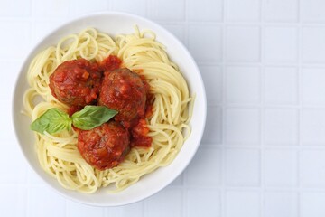 Delicious pasta with meatballs in bowl on white tiled table, top view. Space for text