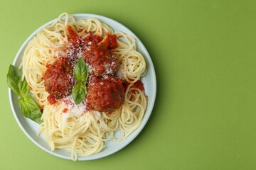 Delicious pasta with meatballs, basil and cheese on green table, top view. Space for text