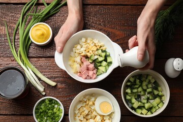 Making okroshka soup. Woman adding salt into bowl with different ingredients at wooden table, top...