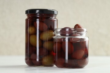 Pickled olives in glass jars on white table, closeup