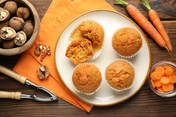 Tasty carrot muffins, fresh vegetables, nutcracker and walnuts on wooden table, flat lay