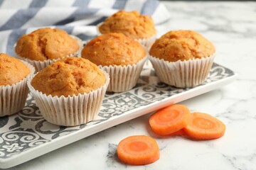 Tasty carrot muffins and cut vegetable on white marble table, closeup