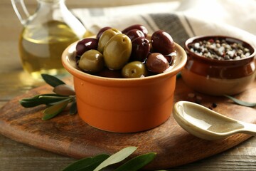 Tasty olives in bowl, leaves and spices on wooden table, closeup