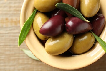 Tasty olives and leaves in bowl on wooden table, top view