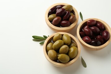 Tasty marinated olives in bowls and leaves on white table. Space for text
