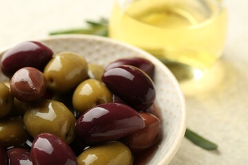 Tasty marinated olives in bowl and oil on beige table, closeup
