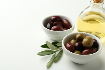 Tasty marinated olives, leaves and oil on white table, closeup. Space for text