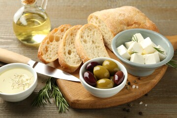 Delicious marinated olives, bread and feta cheese served on wooden table, closeup