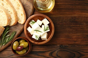 Delicious marinated olives, bread and feta cheese served on wooden table, top view. Space for text