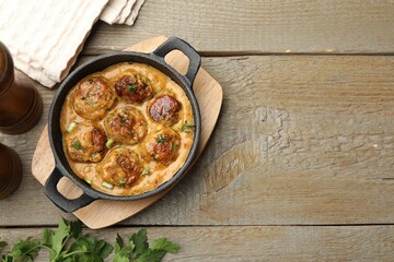 Delicious meatballs with gravy cream sauce and herbs on wooden table, flat lay. Space for text