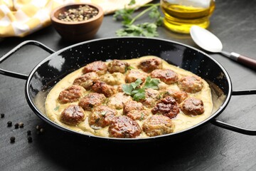 Delicious meatballs with gravy cream sauce and herbs served on black table, closeup