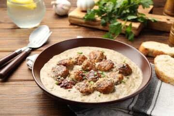 Delicious meatballs with gravy cream sauce and herbs served on wooden table
