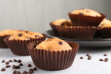 Delicious muffin with chocolate chips on light grey table, closeup