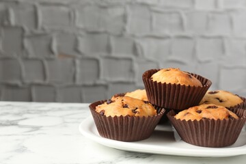 Delicious muffin with chocolate chips on white marble table, closeup. Space for text