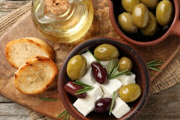 Marinated olives with feta cheese, bread pieces, oil and rosemary on wooden table, top view