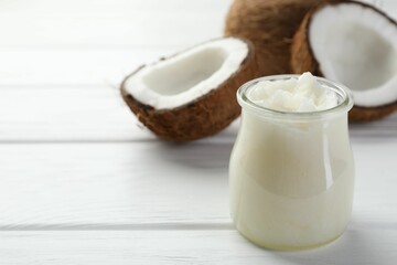 Organic coconut cooking oil in glass jar and fresh fruits on white wooden table, closeup. Space for text