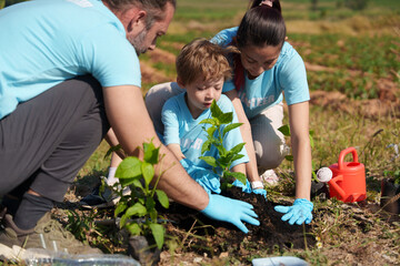 Happy family of father, mother and child are helping each other plant trees on World Warming Day at...