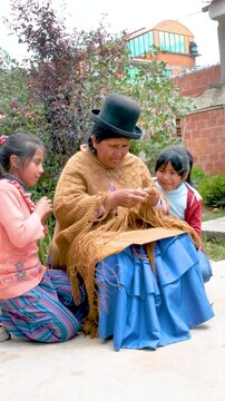 vertical adult aymara woman in pollera working on handcrafted wool textiles with her granddaughters at home in bolivia - work concept