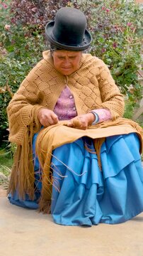 slow motion of vertical adult aymara woman in pollera working on handcrafted wool textiles at home in bolivia - work concept