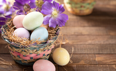 Pastel colored easter eggs in a basket with purple daisies