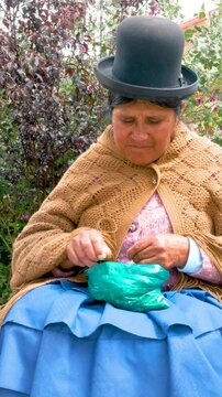 vertical adult aymara woman in pollera consuming coca leaf in the backyard of her house - concept of traditions