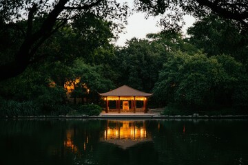 Obraz premium Lit gazebo by pond in tranquil park at dusk