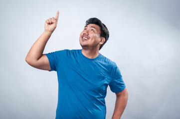 Naklejka premium A smiling Asian man in a blue t-shirt raises his index finger as if making a point or presenting an idea. His confident and engaging expression conveys leadership, innovation, and inspiration