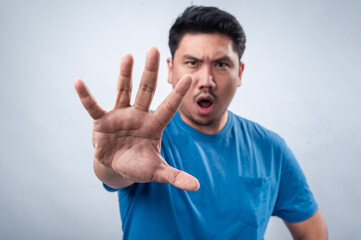 Naklejka premium An Asian man in a blue t-shirt extends his hand forward with his palm open in a commanding 