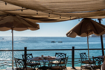 A restaurant by the ocean with tables, chairs, and umbrellas