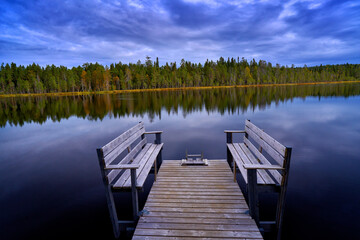 Naklejka premium Autumn landscape from Finland. Pine forest coast with lake and dark blue sky with white clouds. Beautiful scenery from north of Europe.
