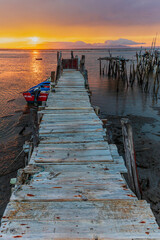 Fototapeta premium An old wooden fishing pier in Portugal in the area of Setubal at sunrise and low tide. Carrasqueira palafitic pier. A dilapidated fishing pier. Torso of a fishing pier. 