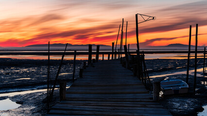 Obraz premium An old wooden fishing pier in Portugal in the area of Setubal at sunrise and low tide. Carrasqueira palafitic pier. A dilapidated fishing pier. Torso of a fishing pier. 