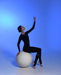 young girl dancer sitting on a ball. Dancer in a black jumpsuit