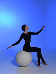 young girl dancer sitting on a ball. Dancer in a black jumpsuit