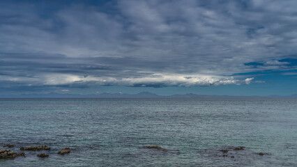 Beautiful calm seascape. Boulders are visible above the surface of the turquoise ocean. Mountains on the horizon. Blue sky, clouds. Madagascar. Nosy Tanikeli   