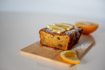Moist homemade orange cake with raisins, garnished with fresh orange slices and powdered sugar, sits on a wooden board, ready to be enjoyed.