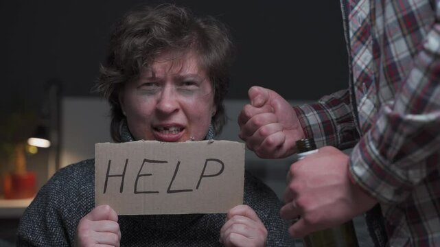 Bruised woman with fear of violence holds HELP sign, pleading for aid. Her face shows injuries, including bruises and broken tooth. Mans clenched fists threaten her, depicting domestic abuse and fear