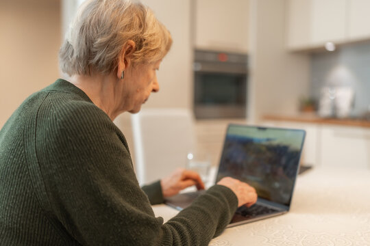Senior woman using laptop at home, looking at the screen and typing on keyboard. Concept of technology, online shopping, digital literacy for seniors and active aging. Technology usage among seniors.