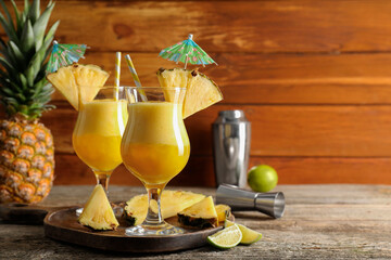 Tasty pineapple cocktail in glasses served on wooden table, space for text