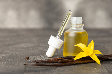 Bottle of vanilla essential oil with vanilla flower on textured background. aromatic vanilla beans. Vanilla extract. Spa concept. Beauty and care. Place for text. Copy space.